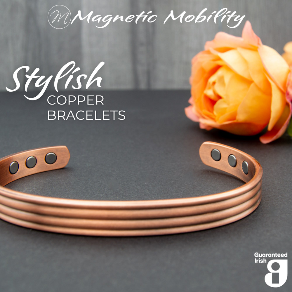 Front view of the Heath Copper bracelet from Magnetic Mobility. The bracelet features a simple design. Featured on a dark surface with a rose in the background signifying its popularity among gardeners for helping with aches and pains. 