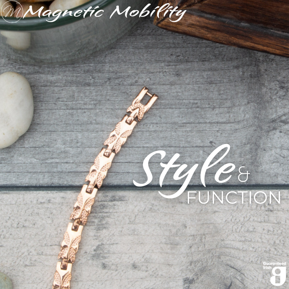 Top view of the Meadowsweet Dawn 4in1 Magnetic bracelet from Magentic Mobility featuring a butterfly design on rose gold stainless steel. The bracelet is shown on a wooden surface. 