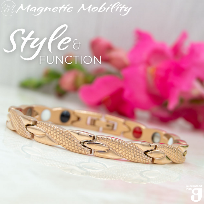 Snapdragon Dawn 4in1 Magnetic Bracelet, rose gold coloured bracelet with snakeskin type designs, designed for pain relief, featuring various therapeutic elements. The bracelet is shown on a reflective surface with a pink flower behind it. 