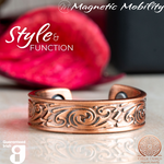 Front view of the Feverfew copper ring by Magnetic Mobility featuring an intricate Irish design. This adjustable ring is designed to be easily worn on arthritic fingers, providing both style and functionality. The image shows the ring in front of a red Christmas decoration. 