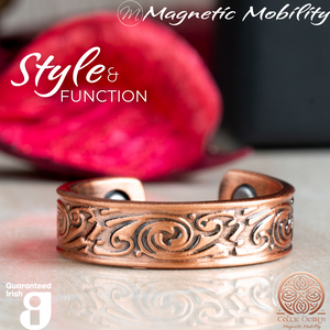 
                  
                    Load image into Gallery viewer, Front view of the Feverfew copper ring by Magnetic Mobility featuring an intricate Irish design. This adjustable ring is designed to be easily worn on arthritic fingers, providing both style and functionality. The image shows the ring in front of a red Christmas decoration. 
                  
                