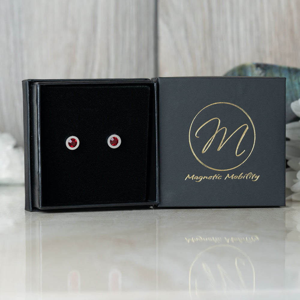 
                  
                    Load image into Gallery viewer, Magnetic Mobility Birthstone Stud Earrings featuring red Swarovski crystals, elegantly presented in a black box with Magnetic Mobility logo. These magnetic back earrings provide stylish pain relief.
                  
                